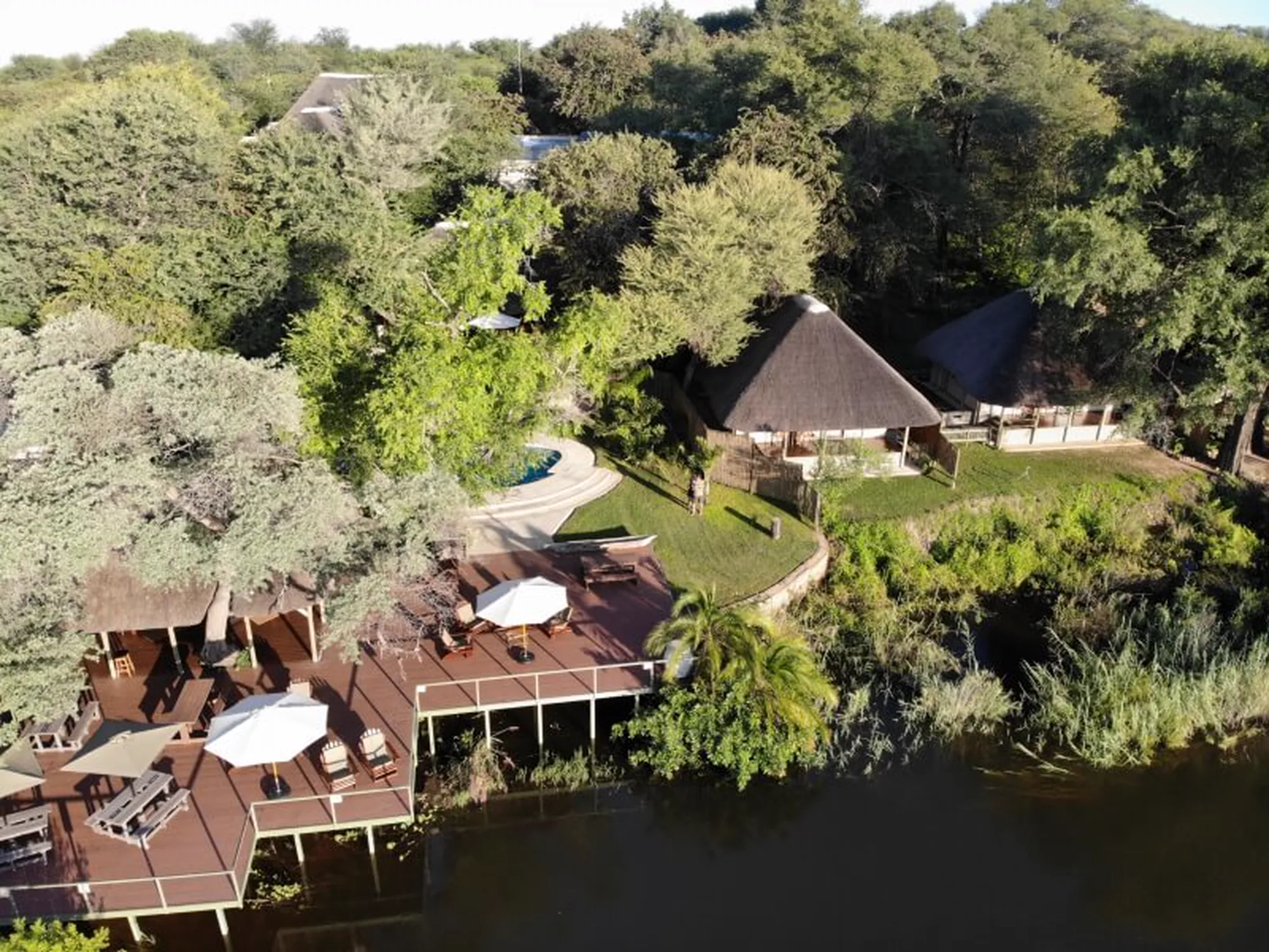 Shametu River Lodge from the air, decks and thatched chalets along the bank